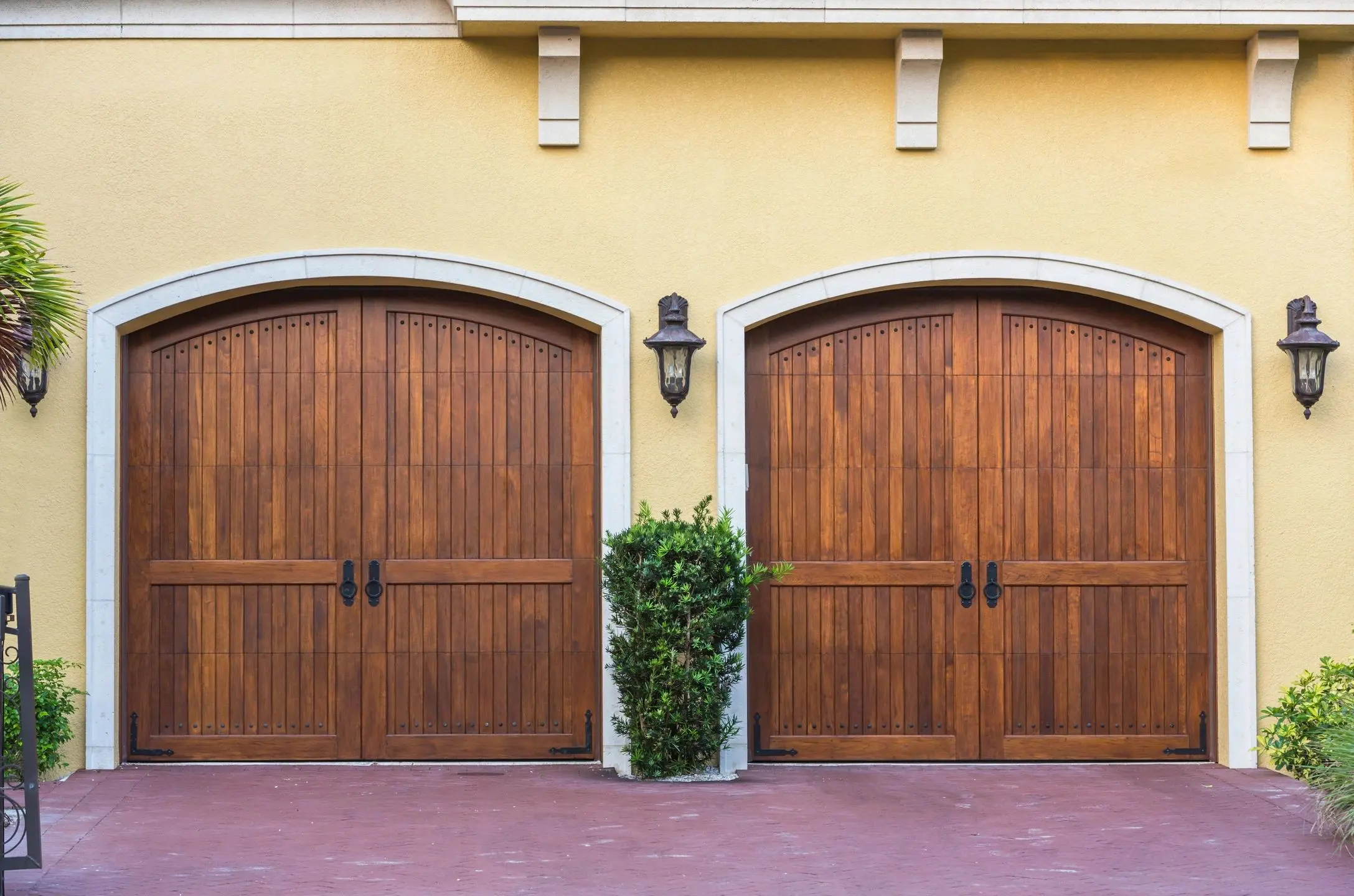 Two wooden garage doors on a yellow house.